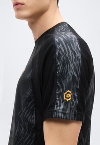 Μαύρο αθλητικό πουκάμισο με υφασμάτινο δίχτυ με υφή, αφηρημένο γκρι σχέδιο στο μανίκι και μικρό χρυσό εξαγωνικό λογότυπο στο χέρι.