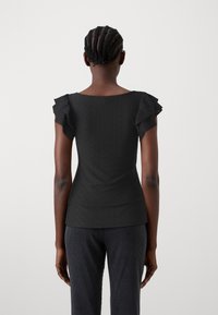 Černý top s krátkými řasenými rukávy, texturovaná látka s diamantovým vzorem, zadní pohled ukazuje přiléhavý střih a hladký výstřih.