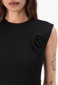 Black textured dress featuring a fitted design and a sculpted rose accent on the shoulder. Short sleeves and a round neckline.