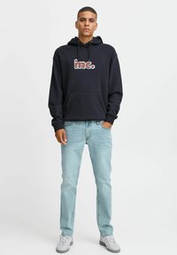 Sudadera navy con logo "inc." en texto multicolor, combinada con jeans de color azul claro y zapatillas blancas, con un corte relajado y bolsillo delantero.