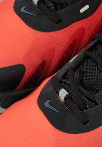 Des chaussures de sport rouges et noires avec une tige texturée, des accents en mesh, un logo Nike distinctif, des lacets noirs et une semelle rembourrée.