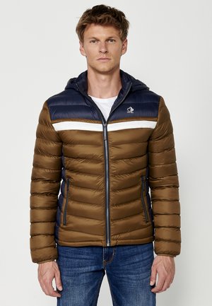 Veste matelassée marron avec une capuche bleu marine, bande blanche sur la poitrine, poches zippées et un logo en haut à gauche.