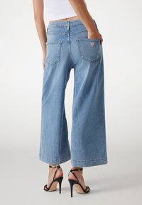 Jeans a vita alta e gamba larga di colore azzurro chiaro, con design a cinque tasche, caratterizzati da un logo a triangolo sulla tasca posteriore. Tessuto denim testurizzato.