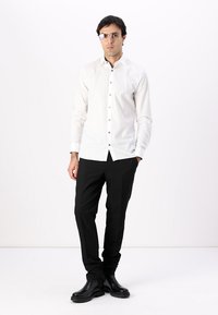 Hvit skjorte med knapp og slim fit, sammen med svarte bukser. Skoene er laget av skinnende svart materiale. Klare briller fullfører stilen.