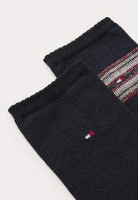 To par med svarte sokker vises, med et mønster av striper i rødt, beige og hvitt nær toppen og en liten logo.