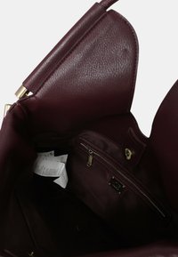 Bordeaux leren handtas interieur met een gladde textuur. Inclusief een ritsvak en een label, met gouden hardware accenten.