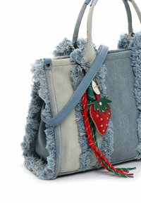 Torba dżinsowa z postrzępionymi jasnoniebieskimi krawędziami, o usztywnionym kształcie, niebieskich uchwytach i ozdobiona czerwoną zawieszką w kształcie truskawki.