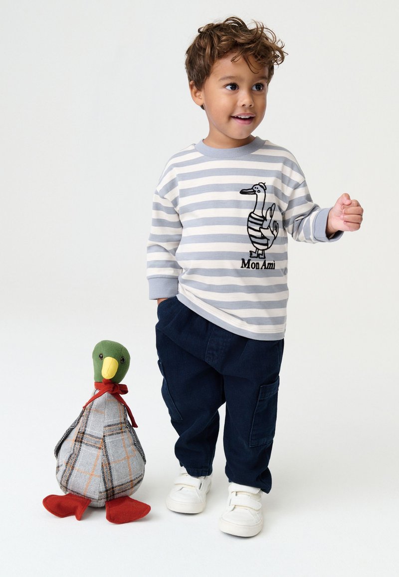 Striped gray and white long-sleeve shirt with duck graphic, paired with dark navy cargo pants and white sneakers. Stuffed duck toy nearby.