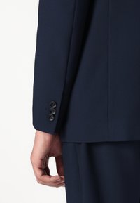 Ärmel eines Marineblazers mit drei schwarzen Knöpfen, glatte Textur, taillierte Passform und sorgfältig verarbeitete Nähte, die ein professionelles Design präsentieren.