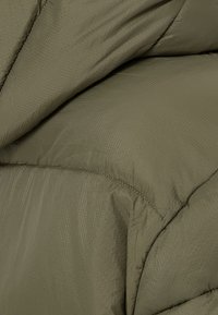 Tkanina kurtki puchowej w kolorze oliwkowej zieleni, o teksturowanym, błyszczącym wykończeniu, z widocznym przeszyciem i miękkim, ocieplonym wyglądem.