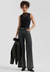 Bodysuit negro sin mangas con detalles de encaje en el escote, combinado con jeans de pierna ancha grises de tiro alto y una chaqueta de cuero negra.
