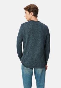 Dunkelblaues Langarmshirt aus strukturiertem Strickstoff, mit Rundhalsausschnitt und lockerer Passform. Kombiniert mit hellblauen Jeans.