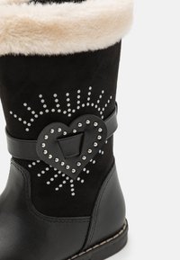 Bottines noires avec doublure en fausse fourrure, décorées d'un ornement en forme de cœur et de détails cloutés sur la tige, en cuir lisse.
