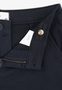 Melni bikses ar rāvējslēdzēju un pogu aizdari, izgatavotas no izturīga auduma. Etiķete redzama iekšējā jostasvietā ar kopšanas norādījumiem.