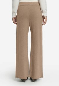 Vidbyxa i mjuk beige tyg, med en slät yta och en ren midja. Längden når anklarna och ramar in skorna.