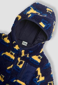 Comoda tuta in pile blu e gialla con cappuccio, dotata di tasca con zip e un motivo di veicoli da costruzione giocosi. Texture morbida in tutto il capo.