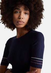 Námořnický vrch s krátkými rukávy z žebrovaného úpletu, s bílými a růžovými pruhy na manžetách. Hladká textura a přiléhavý střih.