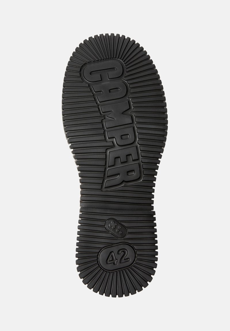 Semelle en caoutchouc noire avec des rainures pour traction, marquée "CAMPER" et taille "42". Surface texturée avec un motif en relief.
