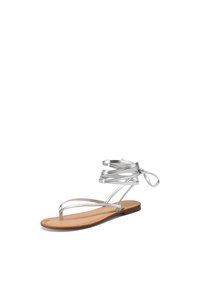 Sandal in argento con cinturini, dotata di suola piatta, caratterizzata da cinturini sottili e un plantare imbottito beige, ideale per l'uso in climi caldi.