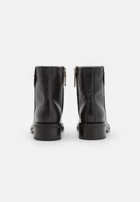 Bottes cheville en cuir noir avec une finition texturée, des fermetures éclair latérales et un petit talon bloc. Le design est simple et moderne.