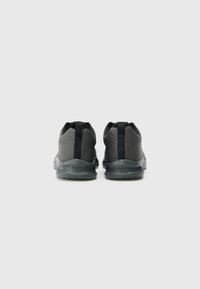 Black athletic shoes featuring a textured upper, padded collar, and rubber sole with ridged detailing. Rear view showcases a pull tab.