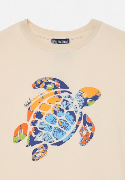 Beżowy T-shirt z kolorowym nadrukiem żółwia morskiego w kwiatowy wzór oraz małym, firmowym napisem obok skorupy żółwia.