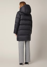 Czarna kurtka puchowa z kapturem, z pikowanym wzorem i długimi rękawami, zestawiona z jasnoszarymi spodniami o szerokich nogawkach i wysokimi obcasami.