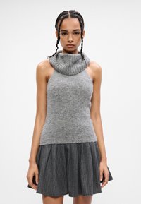 Top in maglia grigia con scollatura a soffietto, abbinato a una gonna nera a righe sottili con pieghe. Texture morbida e design aderente per un look a strati.