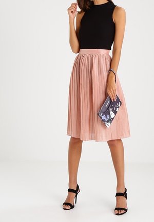 Top nero senza maniche a coste abbinato a una gonna midi rosa plissettata. Accessori includono una pochette con motivo floreale e sandali con tacco neri.