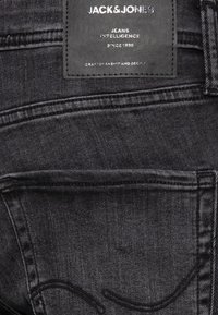 Mustat farkut, joissa on nahkotunnus kohokuvioidulla tekstillä, hienovaraiset ompeleet ja klassinen taskumalli.