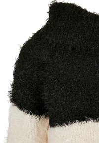 Svart och gräddfärgad fluffig stickad tröja med en texturerad, mjuk yta. Kragen är hög och färgblocken skapar en kontrasterande design.