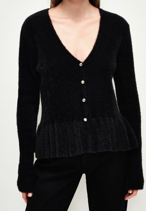 Cardigan noir en tissu pelucheux, avec un décolleté en V profond, cinq boutons en perles et un ourlet à peplum avec texture côtelée. Manches longues.