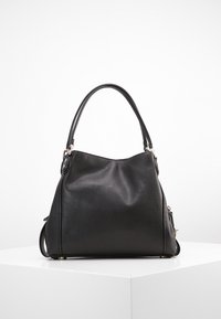 Musta nahkainen käsilaukku, jossa on pehmeä rakenne, kaareva muoto ja lyhyet kahvat. Laidassa on vetoketjullinen tasku ja metalliset yksityiskohdat.