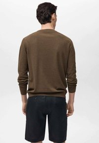 Pull en maille marron avec poignets et ourlet côtelés, associé à un short foncé. Le pull a un col rond et une finition texturée.