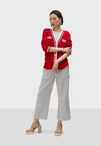 Red ribbed cardigan with white accents, button front. Paired with white and navy striped wide-leg pants and chunky, strappy heels.