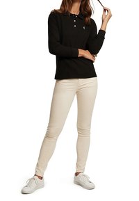 Černá polokošile s dlouhým rukávem a třemi knoflíky, v kombinaci s béžovými skinny džíny a bílými teniskami. Jednoduchý design s malým logem.