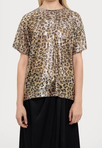 Košile s krátkým rukávem v leopardím vzoru vyrobená z flitrů v zlatých a hnědých tónech, s boxy střihem a kulatým výstřihem, v kombinaci s černou sukní.