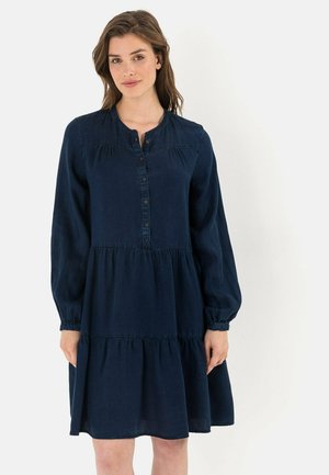 Navyblauwe katoen-twill jurk met een knoopsluiting aan de voorkant, lange mouwen en een gelaagde onderrand. Kenmerkt zich door geplooide details en elastische manchetten.