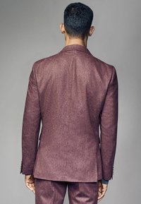 Veste de costume ajustée bordeaux, tissu texturé, revers crantés, fente simple au dos, accompagnée de pantalons assortis.