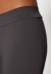 Leggings noirs taille haute en tissu extensible, avec une texture lisse et des coutures nettes, conçus pour le confort et la flexibilité.