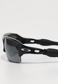 Gafas de sol negras con un diseño elegante, que presentan lentes oscuros, un marco curvado, patillas de goma texturizada y un acento de logo plateado.