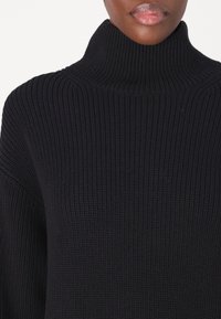 Pull à col roulé noir avec une texture côtelée, une coupe ample et un col haut. Mettez l'accent sur le tissu et les détails du motif tricoté.