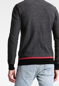 Grauer Strickpullover mit langen Ärmeln, der am unteren Saum einen roten Akzentstreifen sowie einen schwarzen gerippten Bündchen und Saum hat.