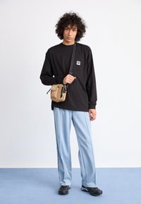 Black long-sleeve shirt with a chest pocket, light blue wide-leg pants, and a beige crossbody bag. Black footwear with textured soles.