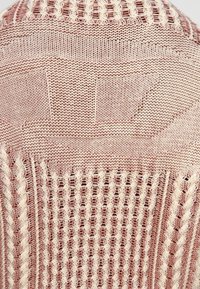 Pull en tricot présentant une combinaison de couleurs rose clair et crème, avec des motifs texturés et des sections en maille ajourée pour une meilleure respirabilité.