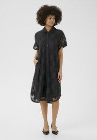 Black lace dress with short sleeves, collar, button front, and floral patterns. Features pockets and a flowy, A-line silhouette.