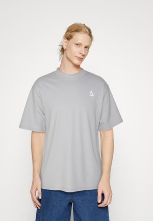 Light gray short-sleeve T-shirt made of soft fabric, featuring a round neck and a small white logo on the left chest. Relaxed fit.