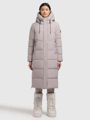 Svijetlosiva duga jakna s podstavom, visokim ovratnikom, dva prednja džepa, podesivim vezicama i detaljima na patentni zatvarač. Uparena s bijelim čizmama.