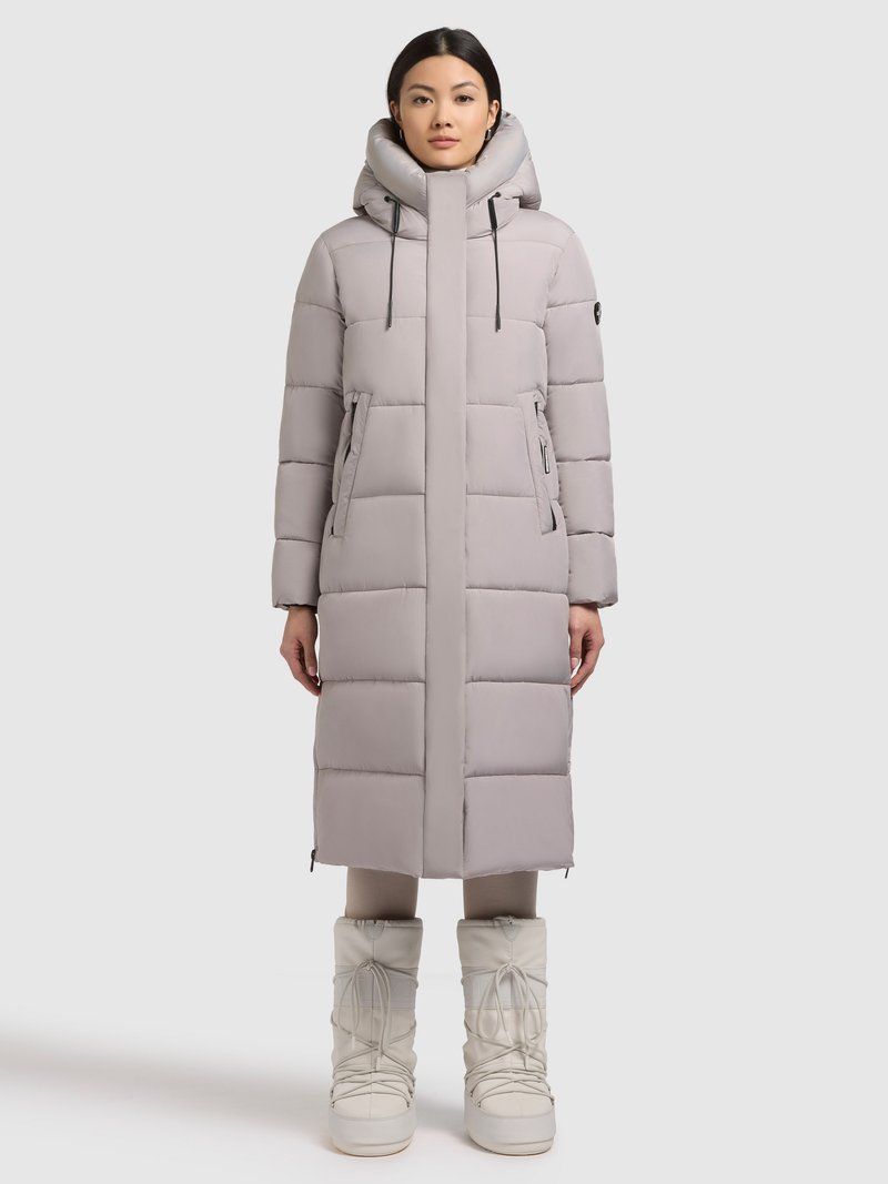 Svetlosivo podložen dolg plašč z visokim ovratnikom, dvema sprednjima žepoma, nastavljivimi vrvico in detajli z zadrgo. Kombiniran z belimi škornji.