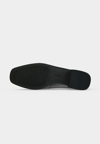 Semelle d'une chaussure en cuir noir avec une accroche texturée à l’avant-pied et au talon, taille 4½, avec le nom de la marque embossé au centre.